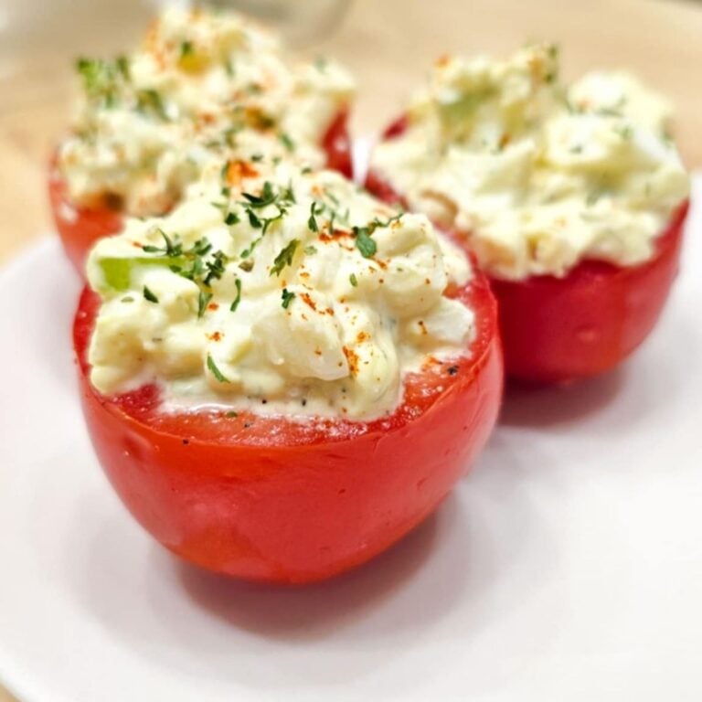 egg salad stuffed tomatoes sitting on a white glass plate on a wooden counter top