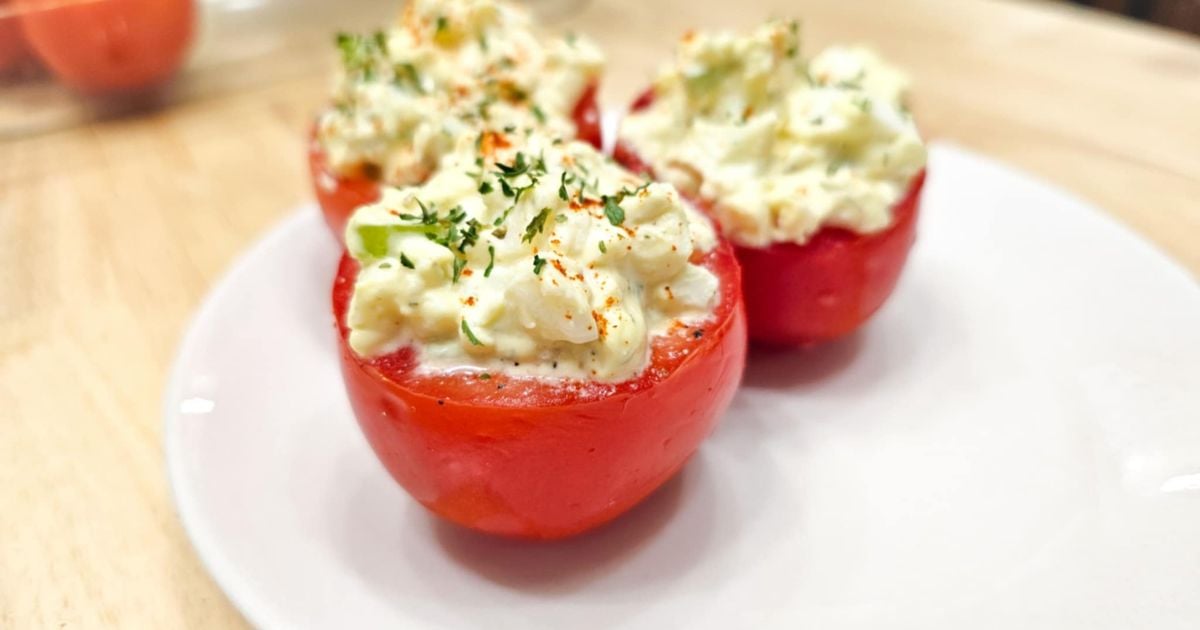 1950s egg salad stuffed tomatoes on a white plate on a wooden counter top