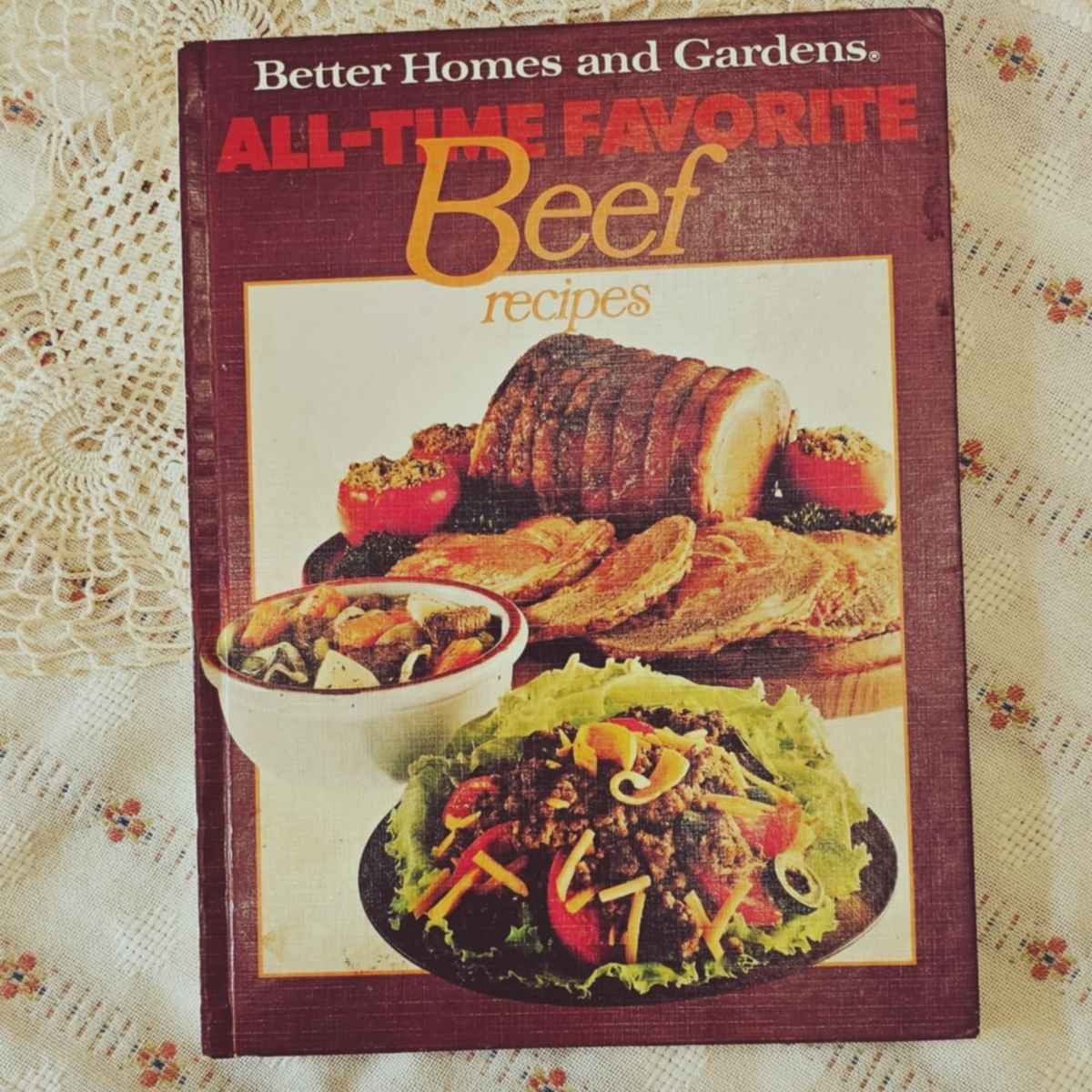 better homes and gardens all time favorite beef recipes cookbook n a vintage table cloth with an old fashioned doily next to it