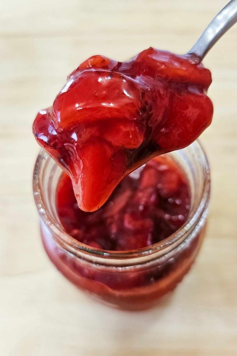 strawberry sauce in a mason jar being scooped out with a spoon