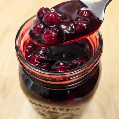 saskatoon berry sauce in a mason jar being scooped out with a spoon