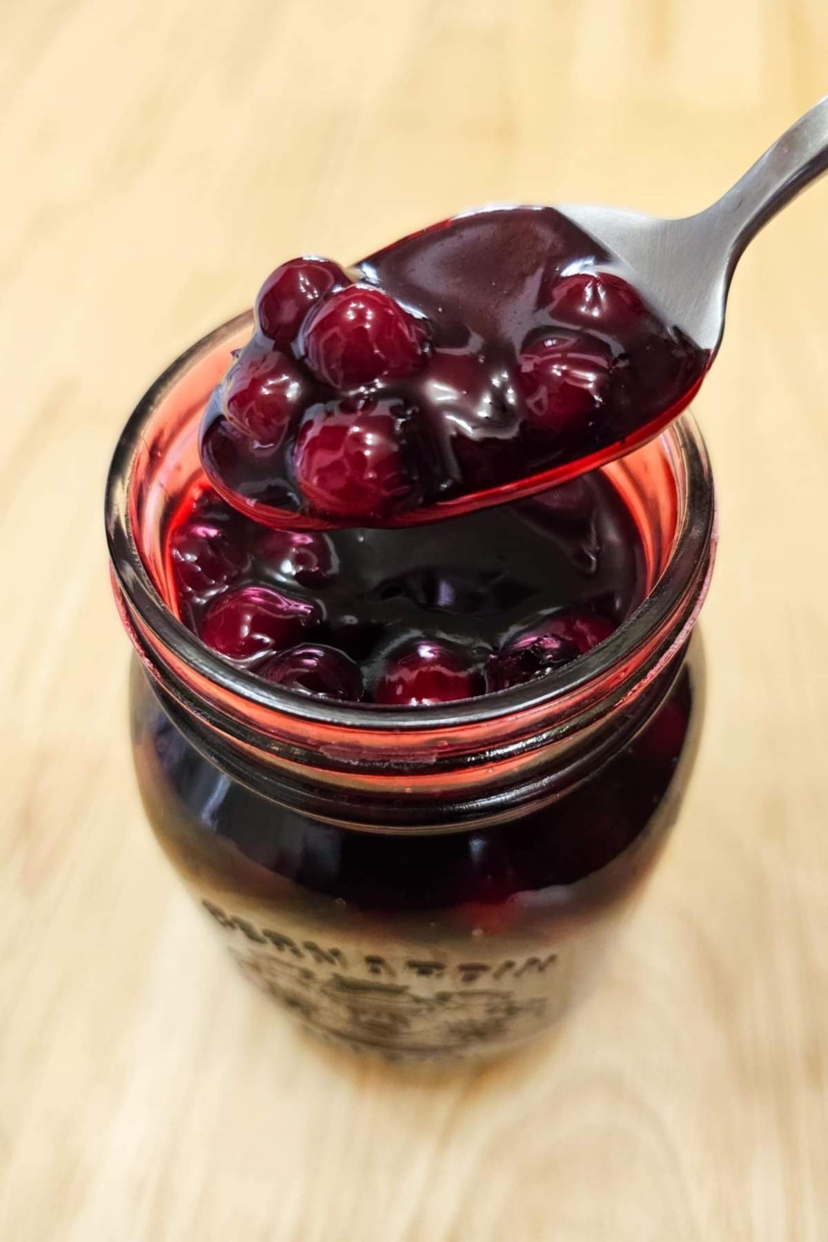 Saskatoon berry sauce in a mason jar being scooped out with a spoon on a wooden counter top