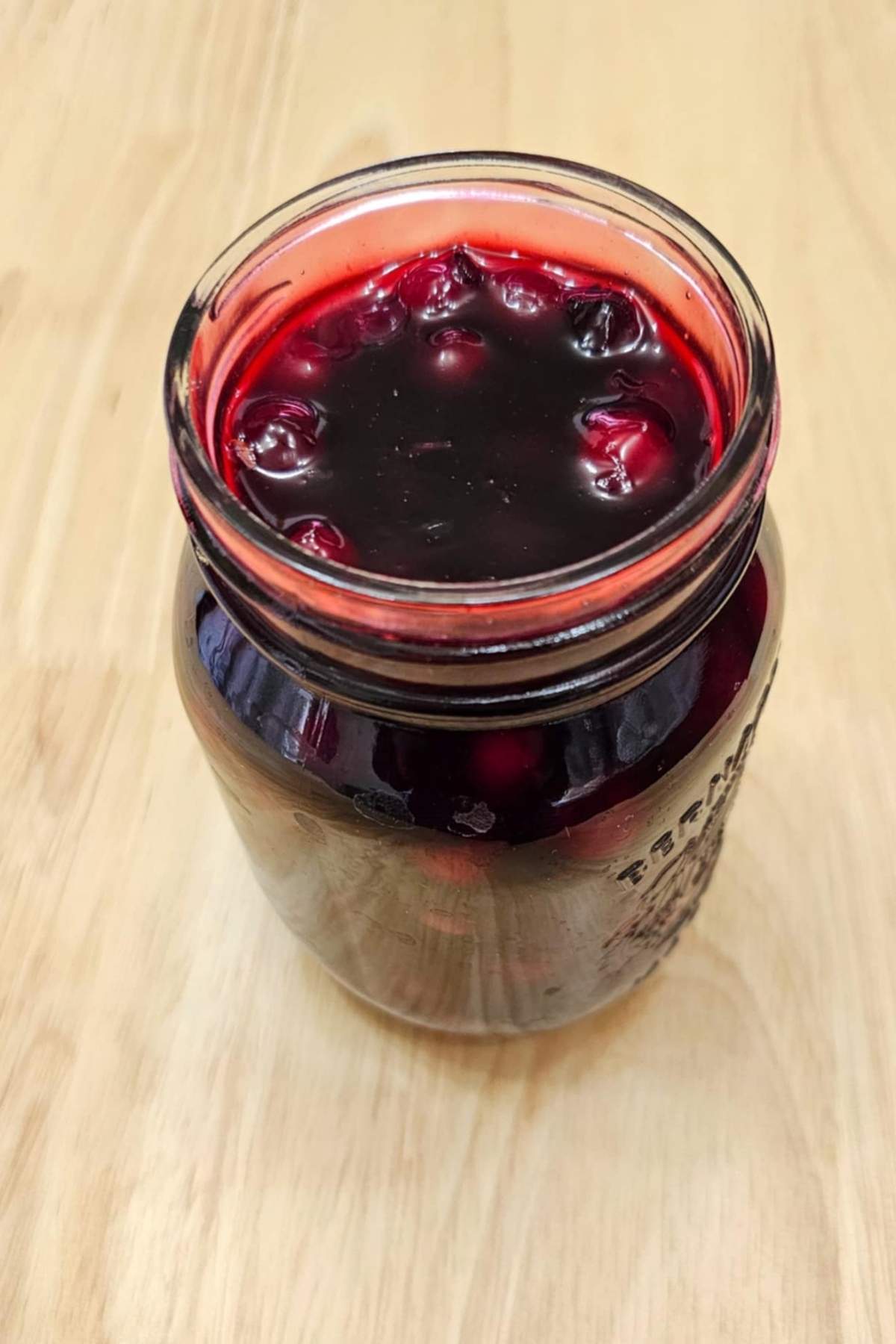 homemade Saskatoon berry sauce in a 500 ml mason jar on a wooden counter top