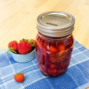 classic strawberry sauce in a mason jar with fresh strawberries next to it on a blue place mat on a wooden table top