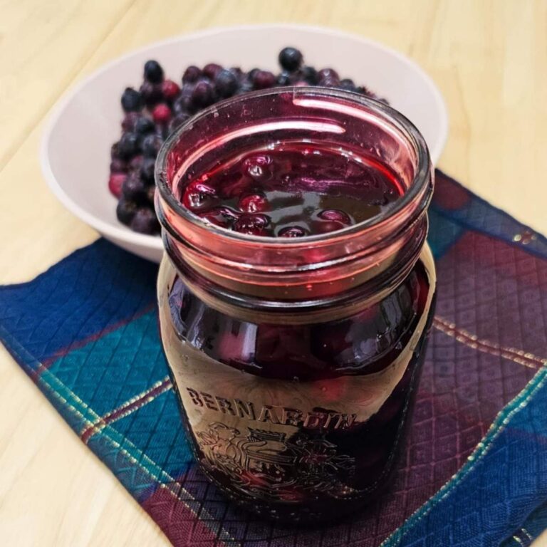 saskatoon berry sauce in a mason jar with berries in the background
