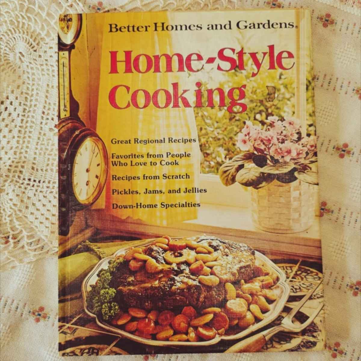 home style cooking better homes and gardens cookbook on a vintage table cloth with a doily to the side of it