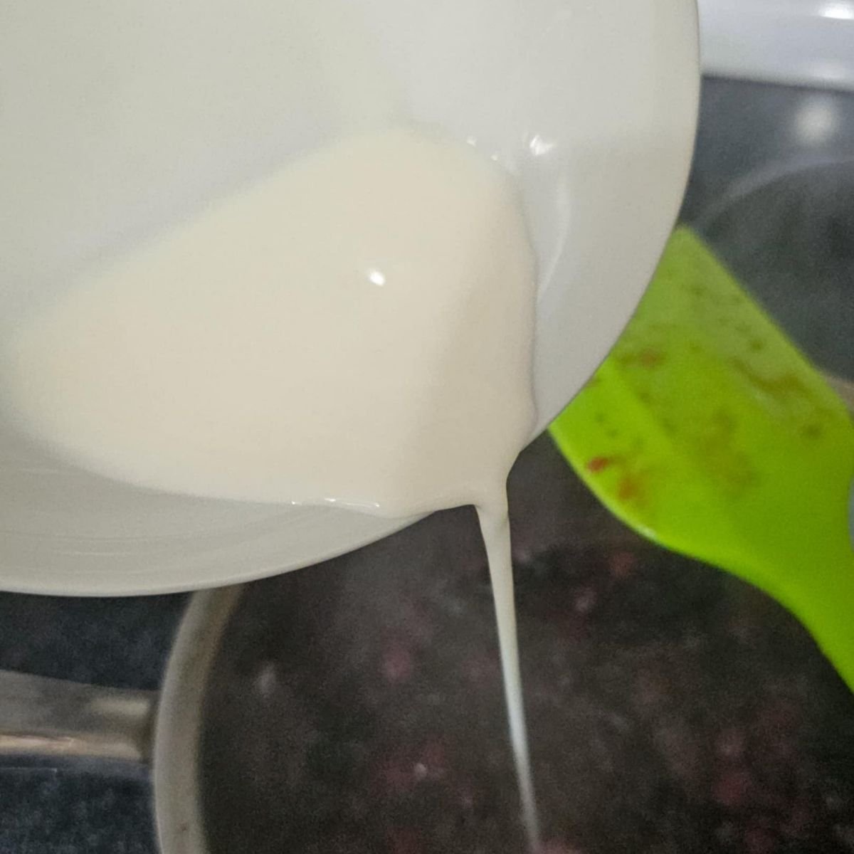 water and cornstarch being poured over Saskatoon berries and sugar and water in a stainless steel pot