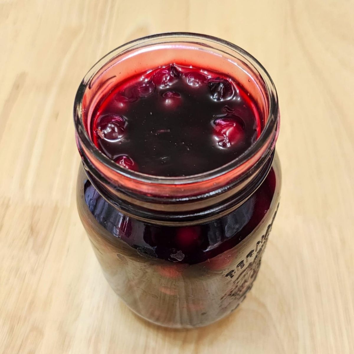 Saskatoon berry sauce in a mason jar on a wooden counter top with the lid off