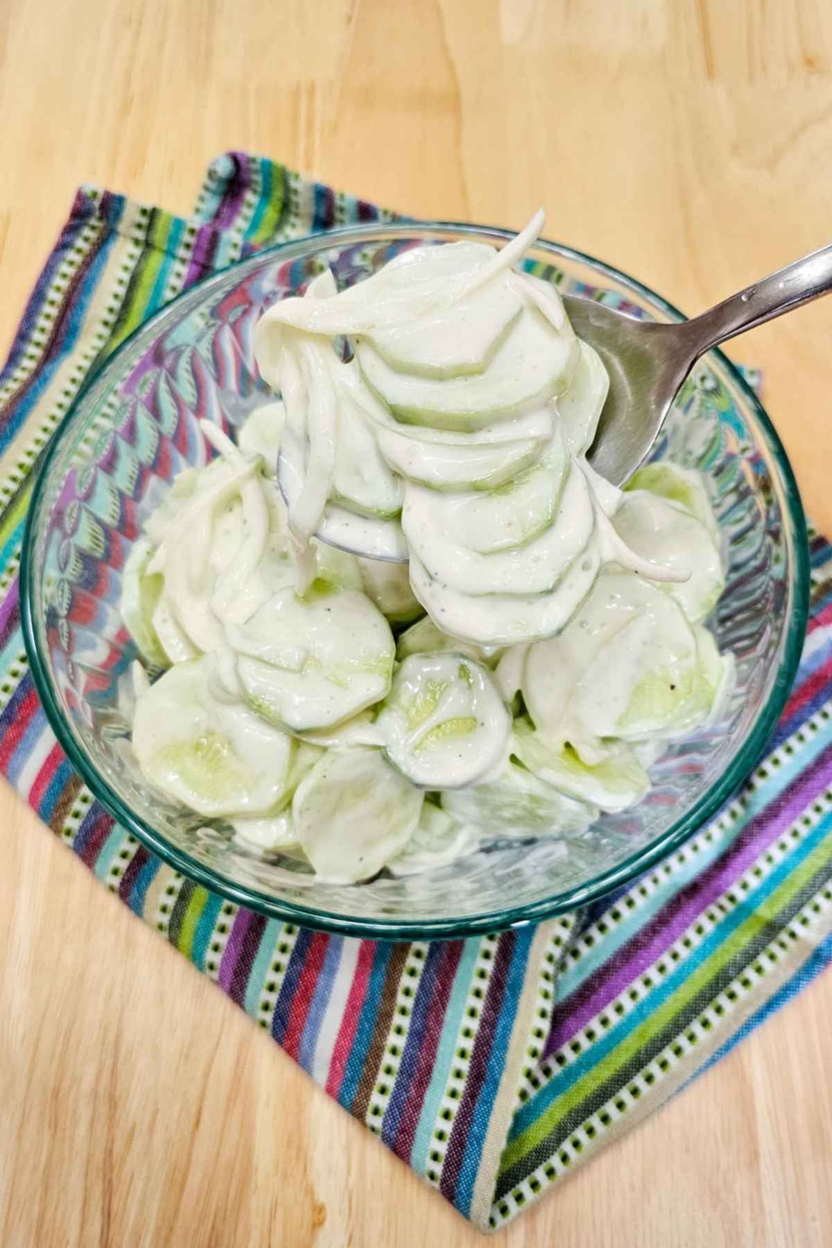 cucumber salad being scooped out of a glass bowl with a large spoon