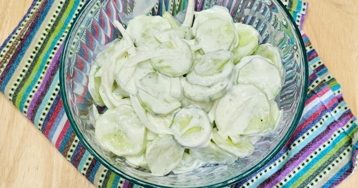 sour cream cucumber salad in a clear glass bowl on a place mat on a wooden counter top