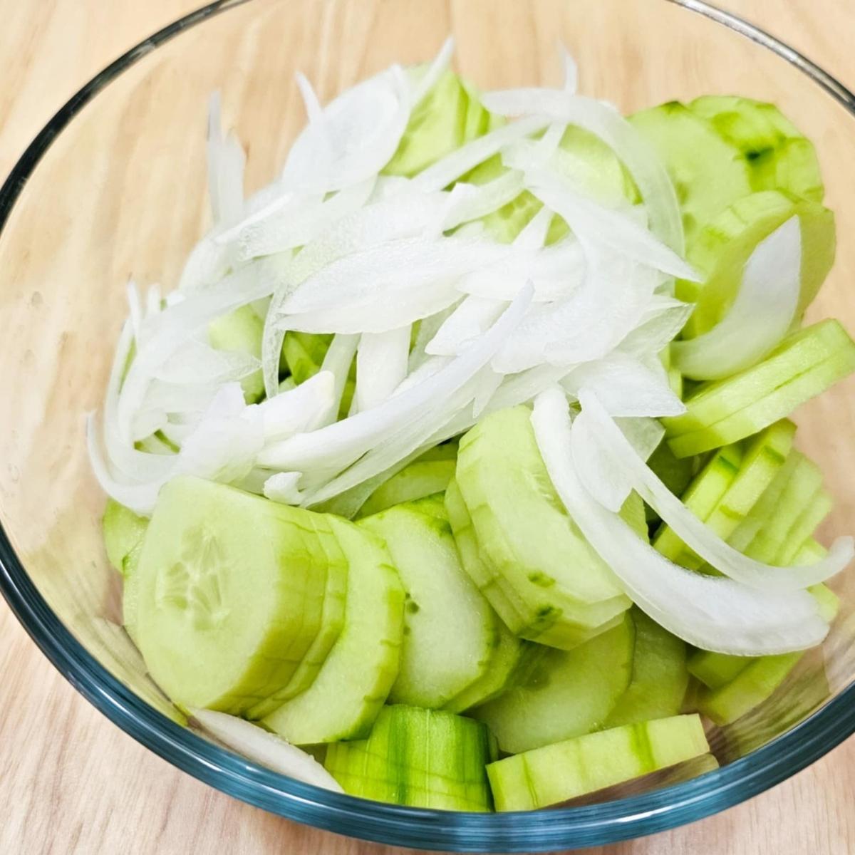 sliced cucumbers and onions in a clear glass bowl