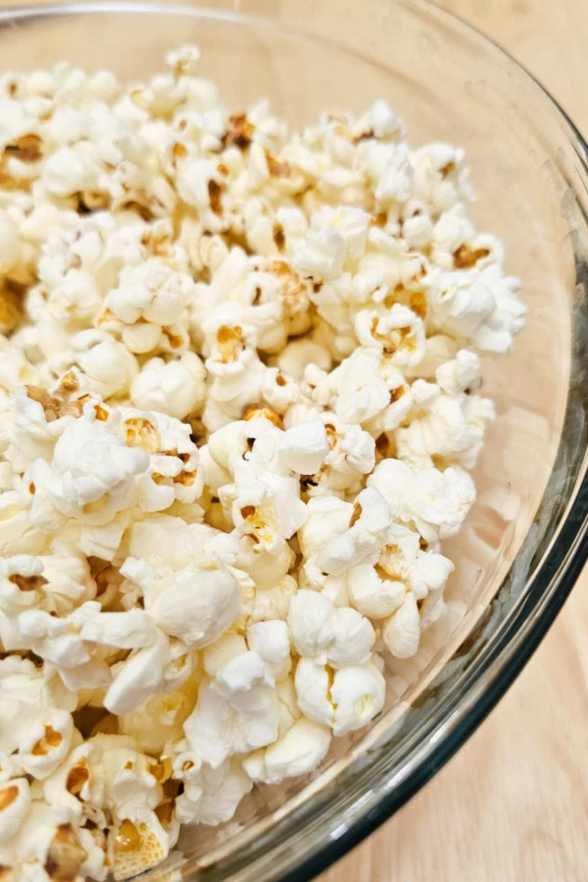 a close up picture of popped popcorn kernels in a large bowl on a wooden counter top