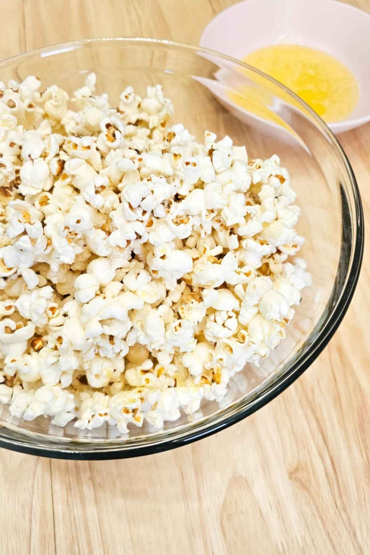 stove top popcorn in a large glass bowl with melted butter in a bowl next to it on a wooden counter top