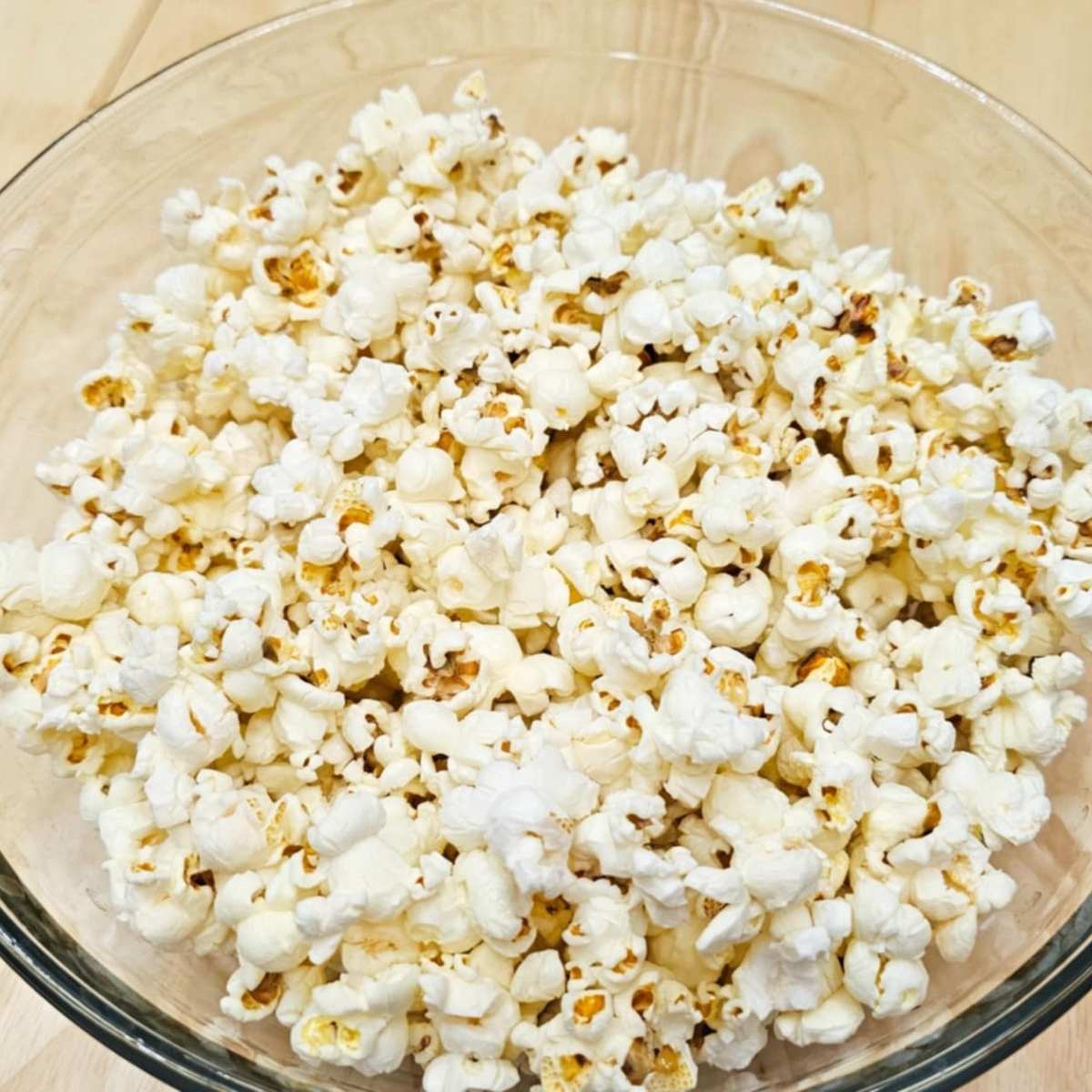 freshly popped popcorn in a clear bowl on a wooden counter top