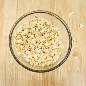 stove top pop corn in a large clear bowl on a wooden counter top with some popped kernels on the counter top
