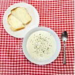 milk soup in a bowl on a vintage table cloth with a spoon next to it and homemade bread