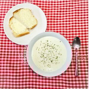 milk soup in a bowl on a vintage table cloth with a spoon next to it and homemade bread