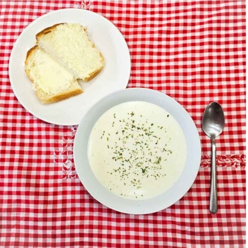 milk soup in a bowl on a vintage table cloth with a spoon next to it and homemade bread