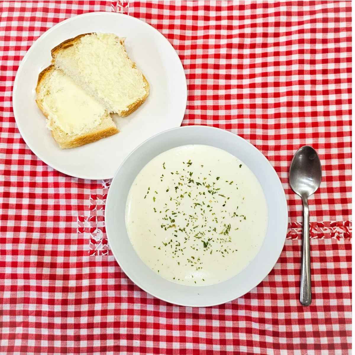milk soup in a bowl, on a red and white vintage table cloth with a spoon next to it and homemade bread with butter