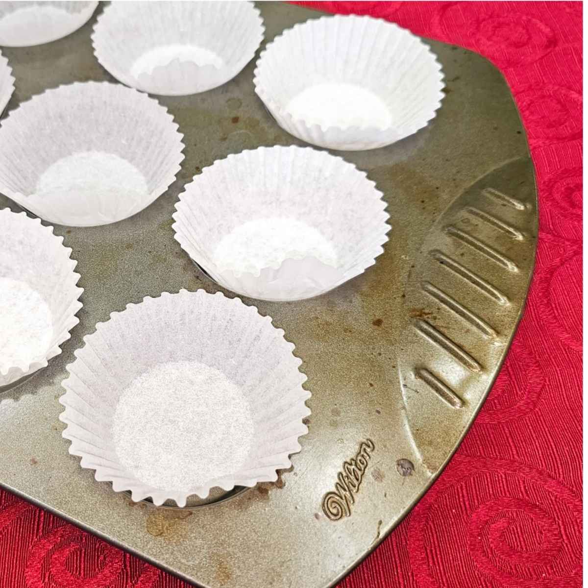 muffin liners in a 12 tin muffin tin sitting on a red vintage table cloth