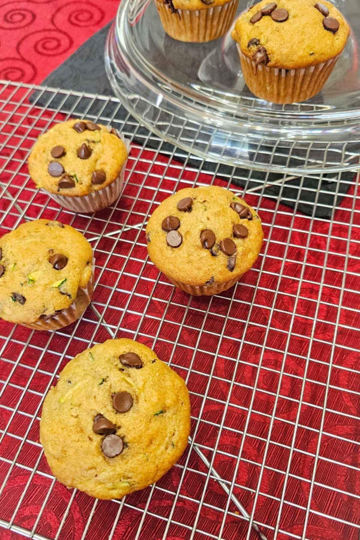 chocolate chip zucchini muffins on a wire rack cooling and sitting on a red table cloth