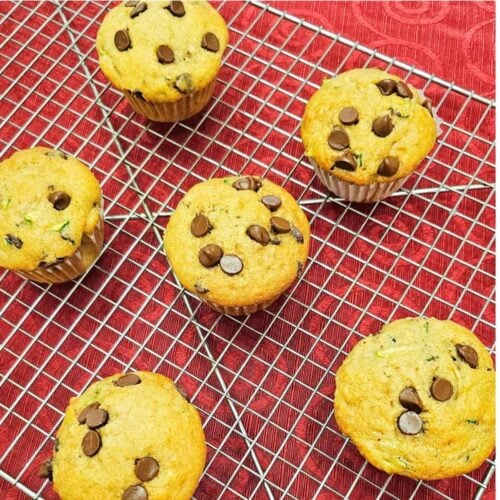 chocolate chip zucchini muffins on a wire rack sitting on a red vintage table cloth