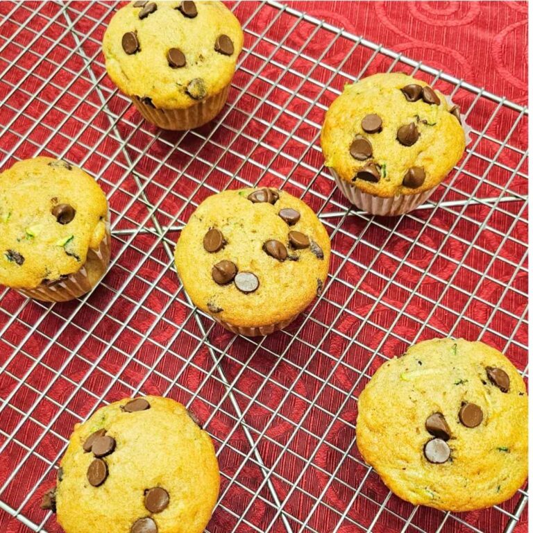 chocolate chip zucchini muffins on a wire rack sitting on a red vintage table cloth