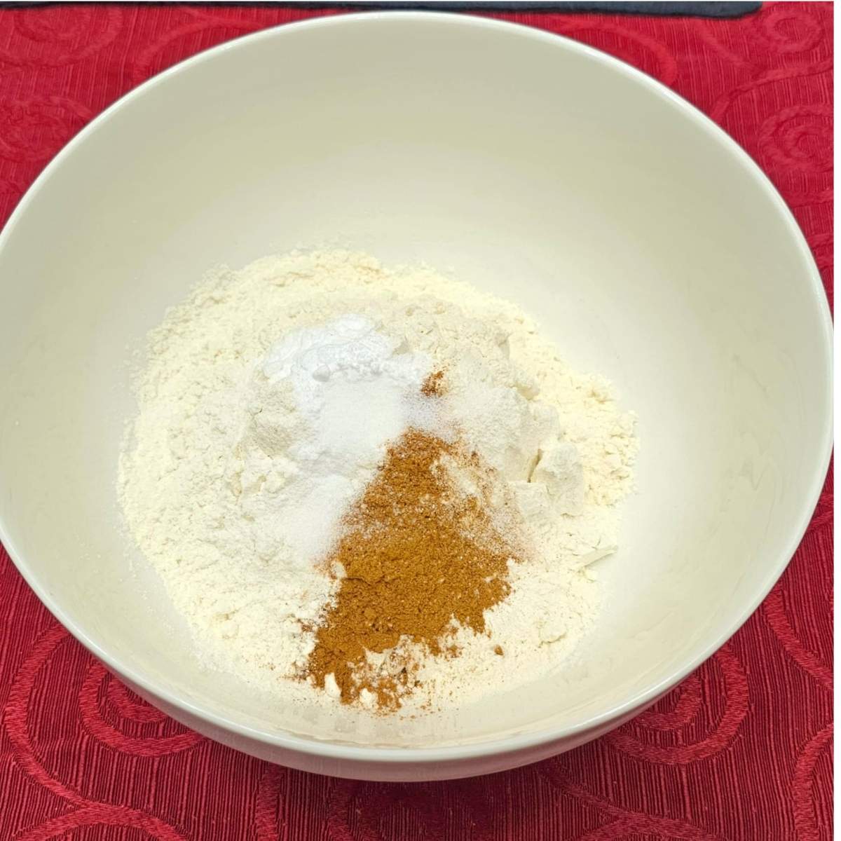 flour, baking soda, salt and cinnamon in a white bowl on a red vintage table cloth