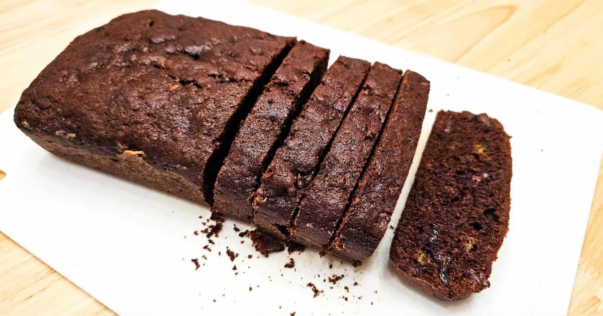 chocolate zucchini bread sliced and sitting on a white cutting board with crumbs from the bread on it