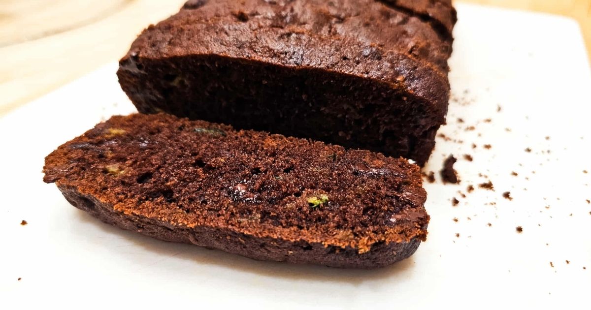 chocolate zucchini bread sliced and close up on a white cutting board with crumbs from the loaf around it