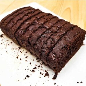 chocolate zucchini bread sitting on a white cutting board with crumbs from the loaf and sliced