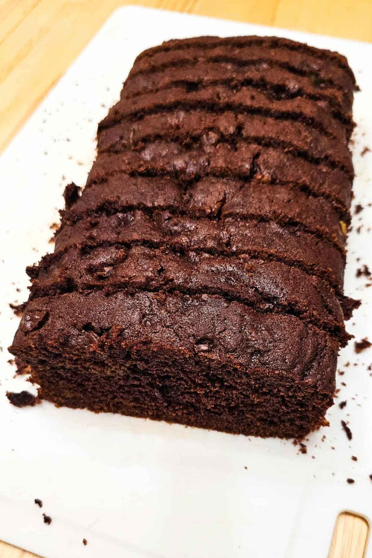chocolate zucchini bread sliced and sitting on a white cutting board with crumbs on it form the bread