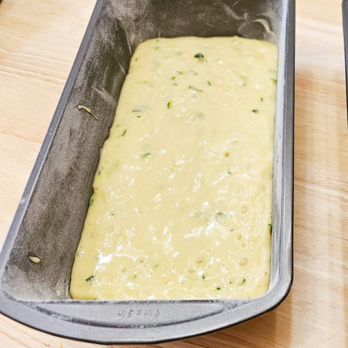 lemon zucchini bread batter in 2 loaf pans sitting on a wooden counter top