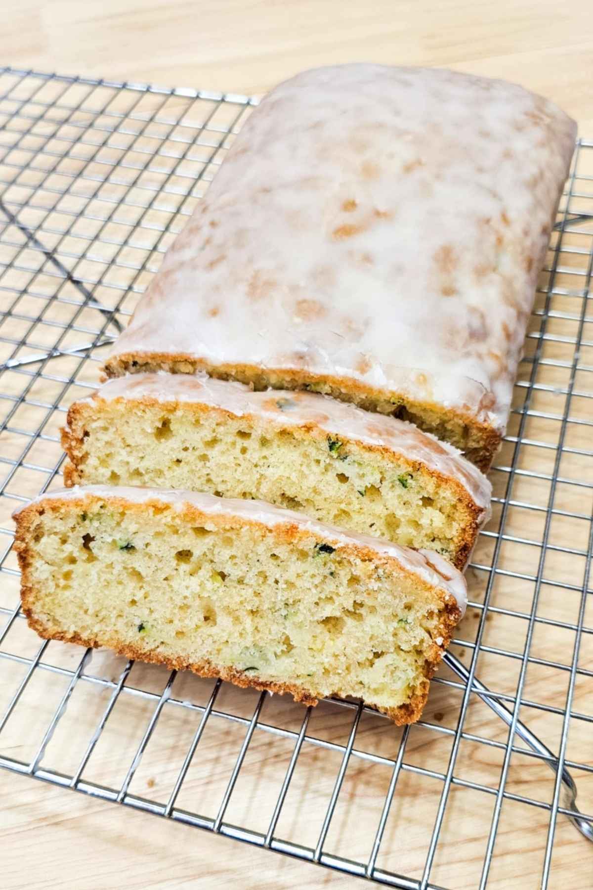 lemon zucchini bread on a wire rack thats is glazed with a lemon glaze and sliced