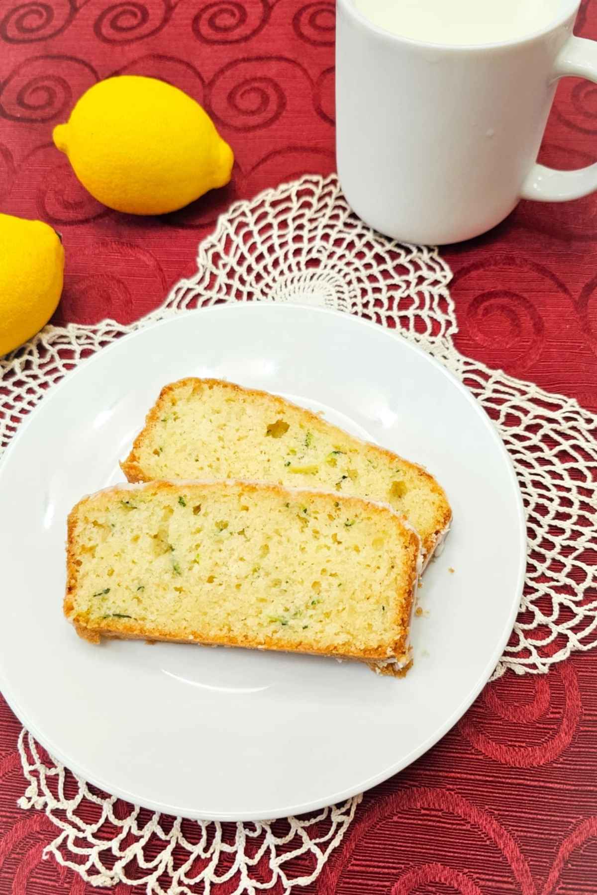 two slices of grandmas lemon zucchini bread on a white plate with a doily in the back on a red table cloth
