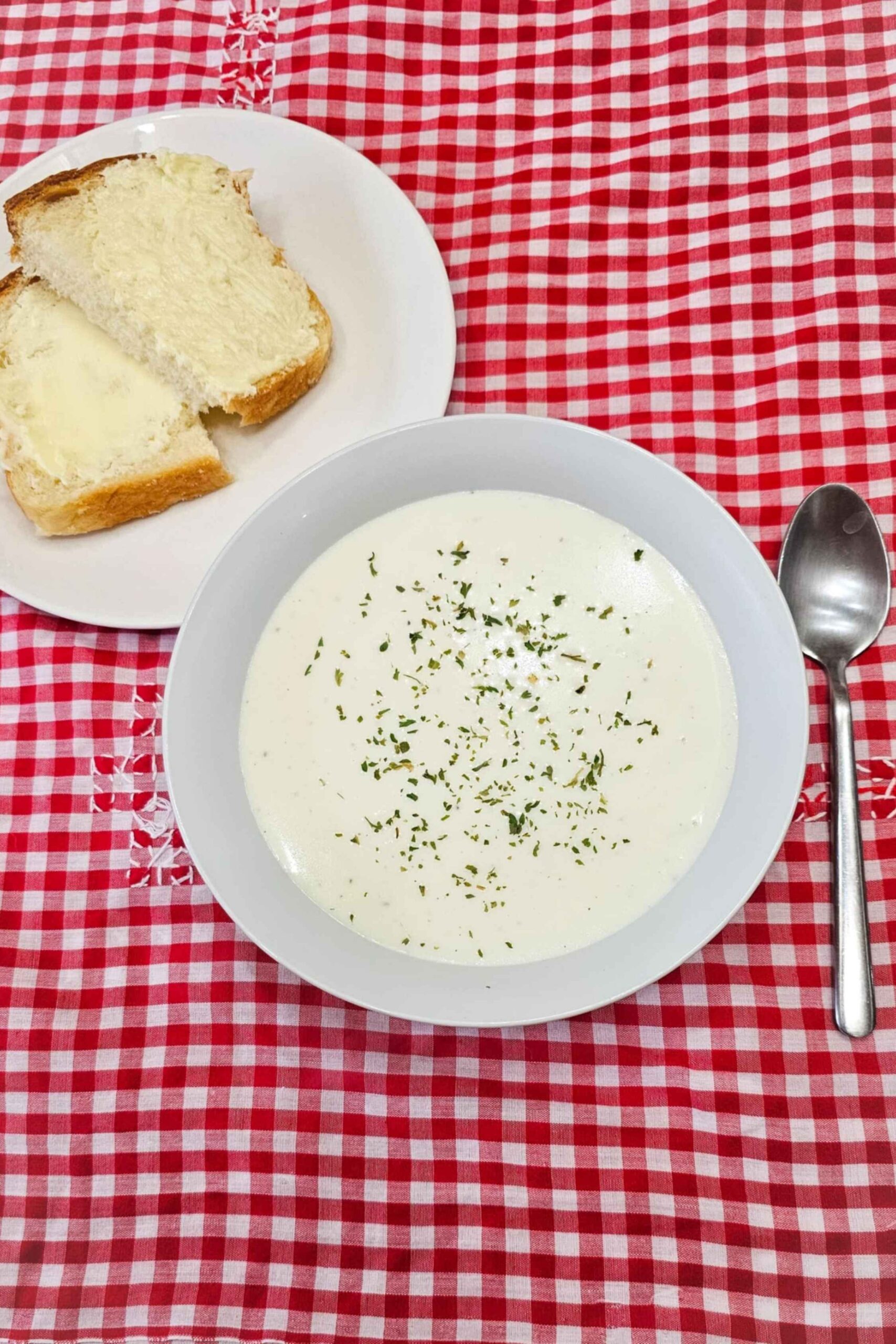 1940ès milk soup in a white glass bowl sitting on a vintage red and white checkered table cloth with a spoon next to it and a dessert plate with homemade bread on it sliced in half
