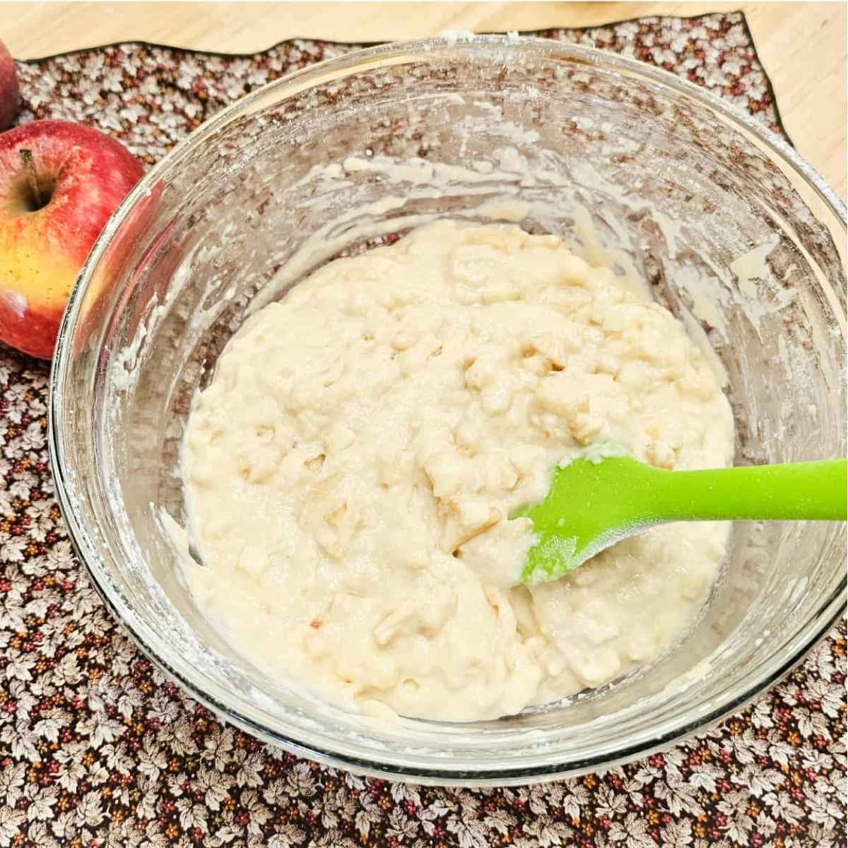 apples folded into the cake batter sitting on a fall cloth napkin with a fresh apple to the side 