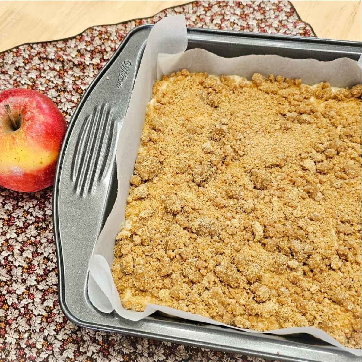 old fashioned apple cake topped with a buttery crumble sitting in a pan on a fall cloth napkin