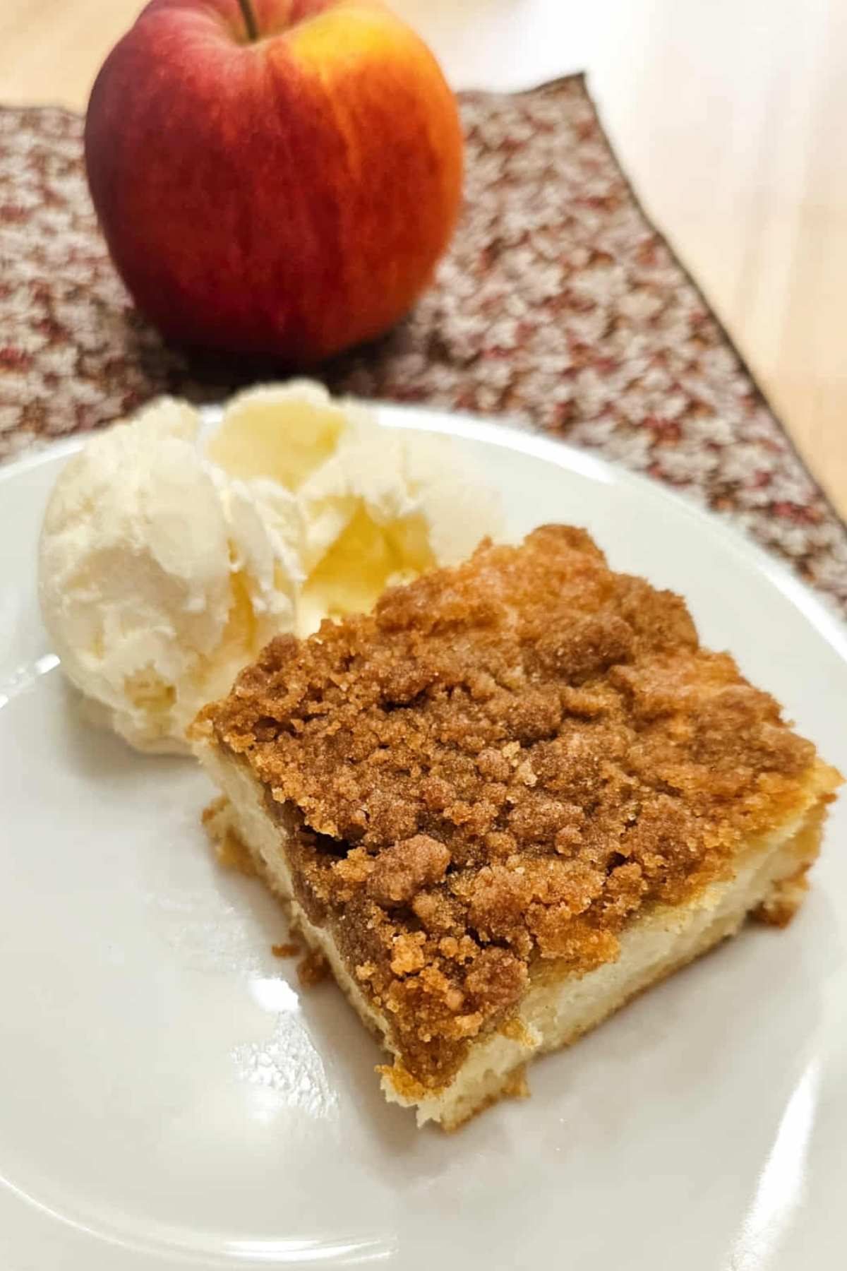old fashioned apple cake on a white plate with a scoop of vanilla ice cream next to it and an apple to the side