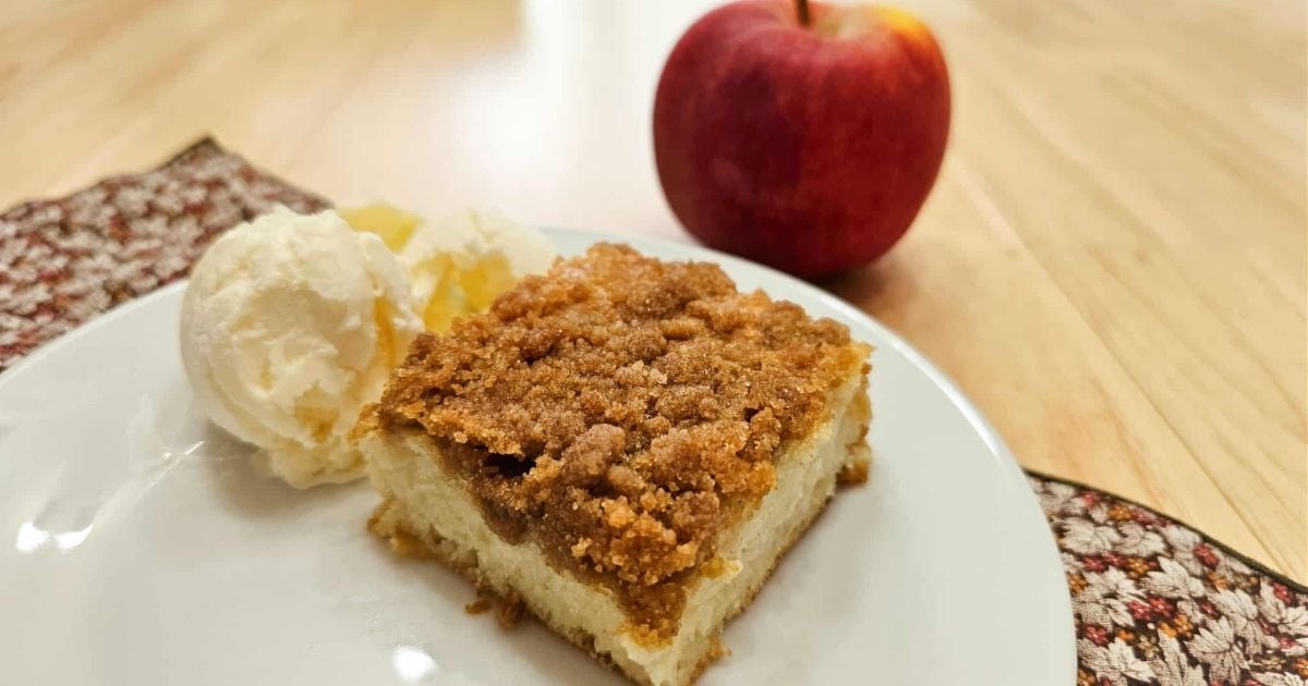 a slice of apple cake sitting on a white plate with a scoop of vanilla ice cream to the side of it with a fresh apple