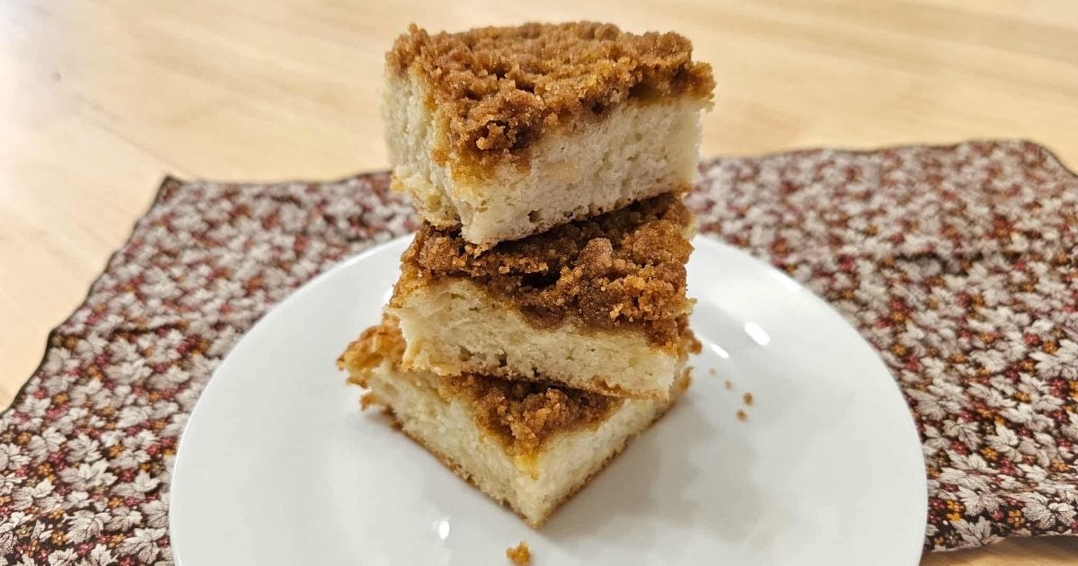 three slices of cake piled on top of each other on a white plate with some crumbs to the side with a fall cloth napkin