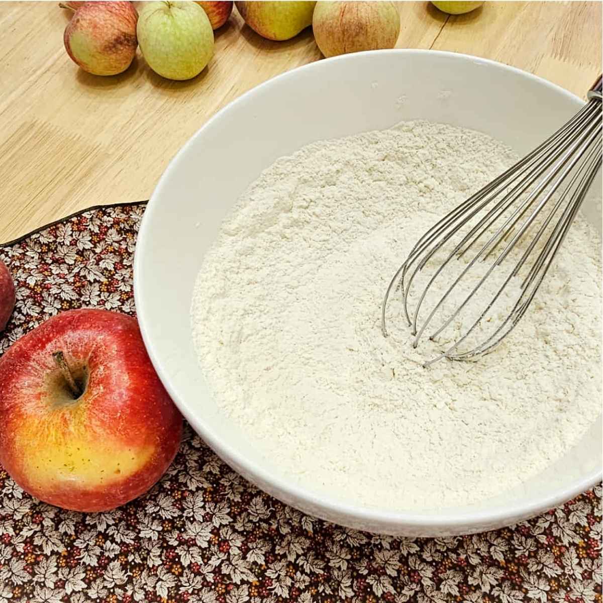 flour, baking powder and salt in a bowl on a fall cloth napkin with an apple to the side of it sitting on a wooden counter top