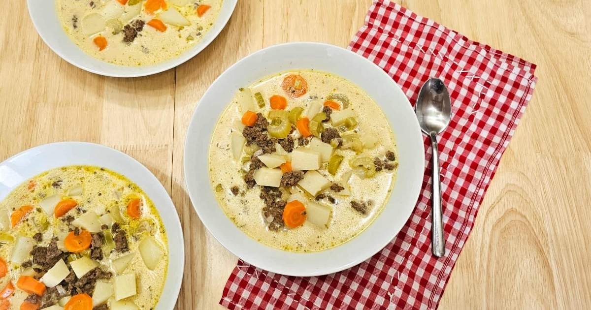 three bowls of cheeseburger soup on a wooden table with a spoon to the side of it sitting on a red and white checkered cloth napkin