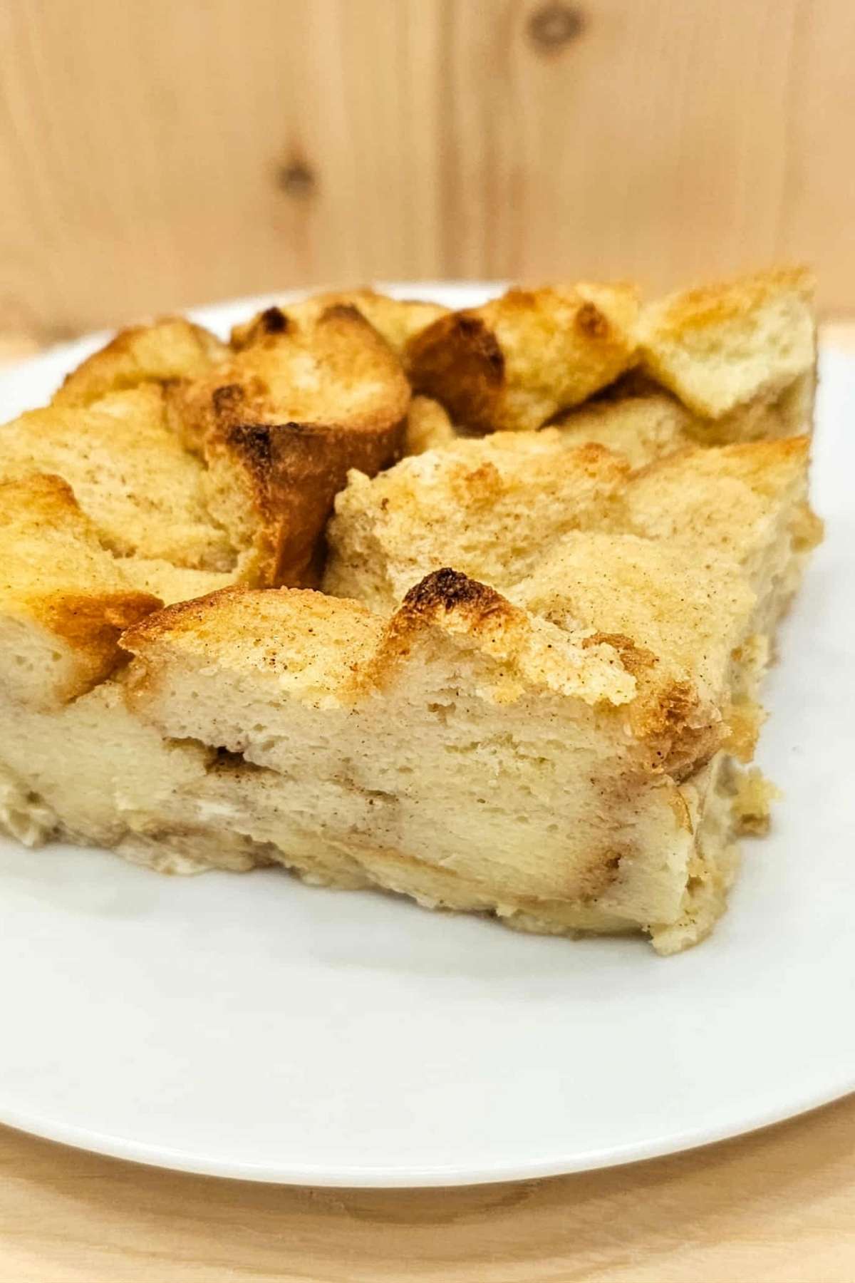 bread pudding sitting on a white plate with a wooden background, close up picture that shows the cinnamon in the bread
