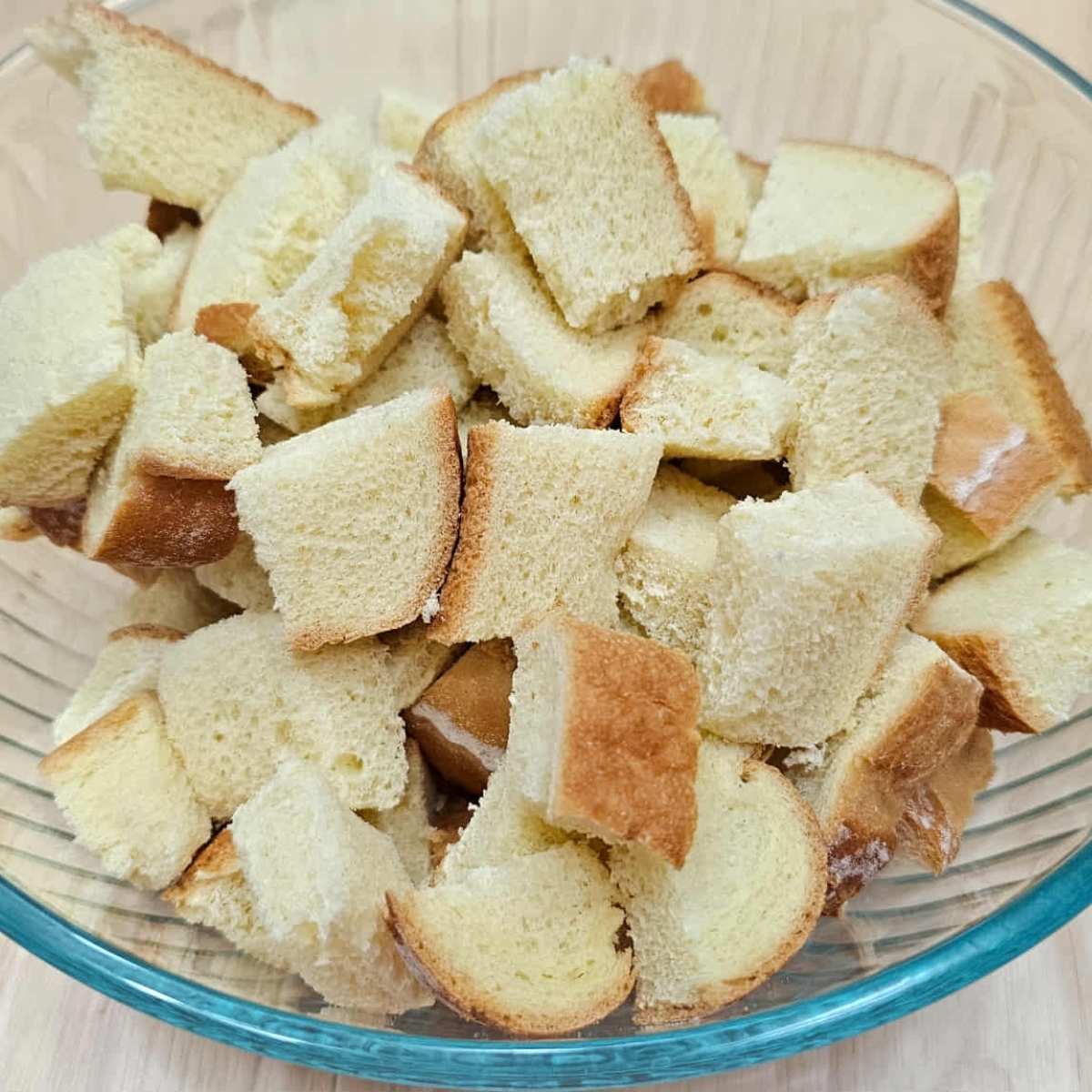 Bread sliced into large cubes, sitting in a clear glass bowl on a wooden counter top