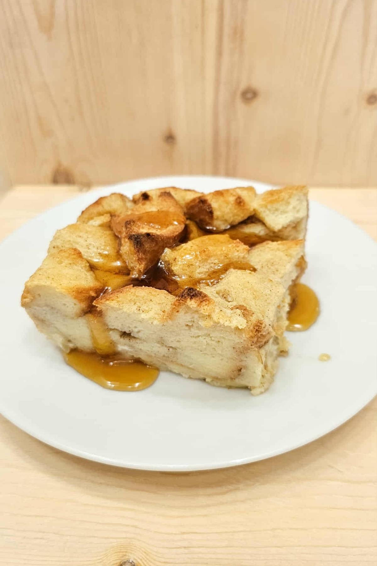 bread pudding with pure maple syrup drizzled over it, sitting on a white plate with a wooden background, close up picture