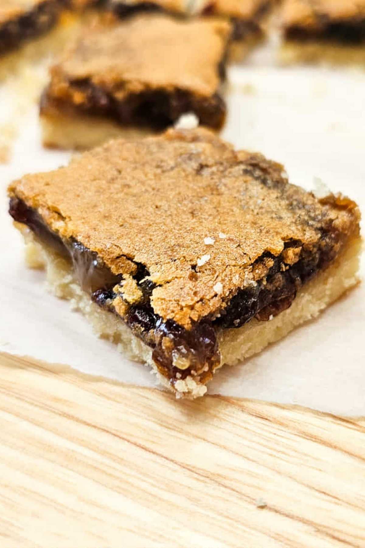 A close up picture of a butter tart square with the filling gooey and sitting on a piece of parchment paper