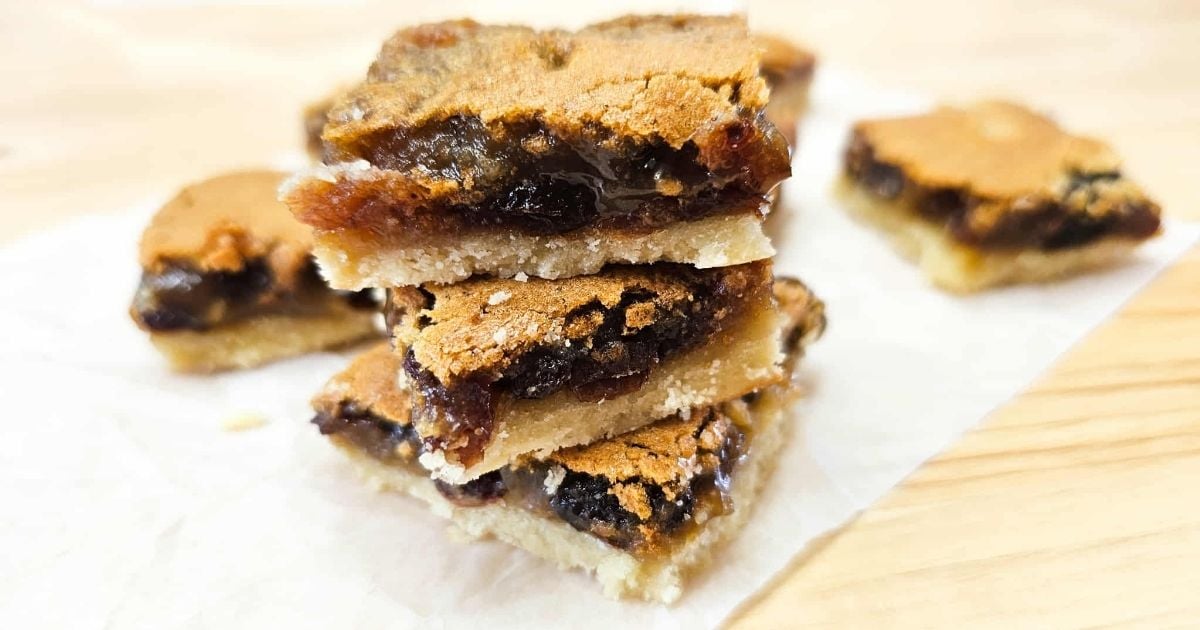 3 butter tart squares piled on top of each other with two in the background on parchment paper on a wooden counter top