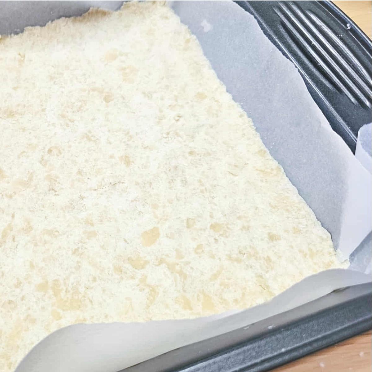 butter tart squares crust in a 9x9 pan sitting on a wooden counter top