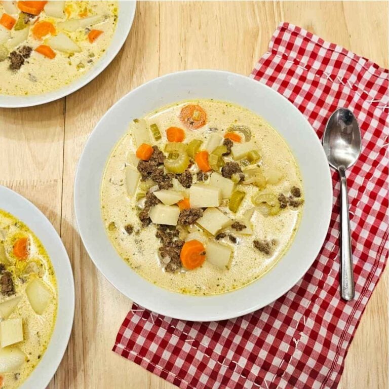 cheeseburger soup in 3 different white glass bowls sitting on a red and white checkered cloth napkin on a wooden table